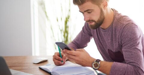 Jeune homme recevant un sms rappel de rendez-vous et le notant dans son agenda.